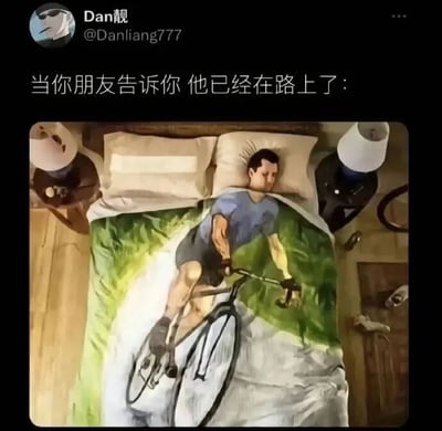 这是一张社交媒体截图，上方有用户“Dan靓”发布的文字“当你朋友告诉你 他已经在路上了：”，下方配图是一个人躺在床上，身上盖着一条印有骑自行车者图案的毯子，毯子上的图案让躺在床上的人看起来像是正在骑自行车赶路，形成幽默反差，调侃朋友说“已经在路上”但实际可能还在休息的情况。