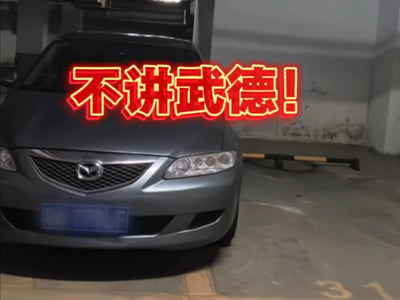 图片展示了一辆灰色马自达汽车停在停车场内，车头朝向镜头，车牌号部分模糊。图片上方叠加了醒目的红色立体文字‘不讲武德!’，字体粗大且带有发光效果，十分抢眼。该梗源自2020年马保国比武失败后的控诉视频，此处通过将‘不讲武德’文字与汽车结合，幽默调侃可能存在的不按常理出牌或出乎意料的情况（如停车方式等），带有明显的网络搞笑意味。