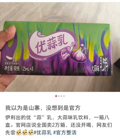 图片展示了一只手拿着一盒名为“优蒜乳”的大蒜味乳饮料，包装盒采用绿色和紫色渐变的泼墨风格设计，中央有“优蒜乳”字样和一个卡通大蒜图案，旁边还有一个夸张的表情图案。包装侧面标注“净含量/规格：125mL×8”和“大蒜味乳饮料”字样。图片下方配有文字说明：“我以为是山寨，没想到是官方 伊利出的优‘蒜’乳，大蒜味乳饮料，一箱八盒。官网店说全国卖2万箱，还没开喝，网友们先尝🧄🧄🧄#优蒜乳 #官方整活”。