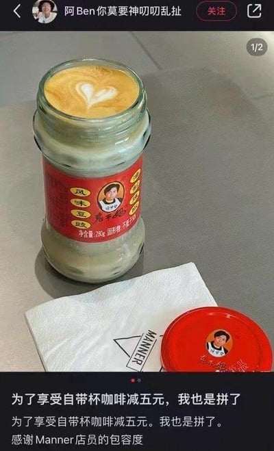 网友为了享受Manner咖啡自带杯减5元的优惠，将吃完的老干妈风味豆豉玻璃罐子清洗后用来装咖啡，罐中的咖啡还带有爱心拉花，旁边摆放着Manner的纸巾和老干妈瓶盖。配文调侃自己为了五元优惠拼了，感谢店员的包容，画面充满生活趣味，把日常省钱操作玩出了新花样，没有双关或谐音梗。