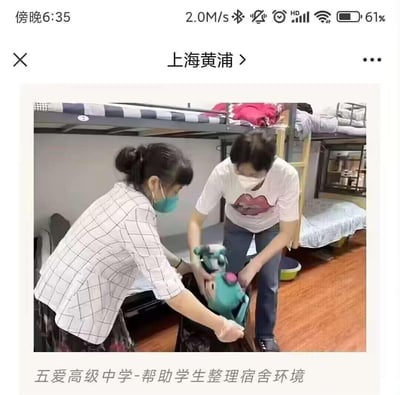 这是一张手机屏幕截图，显示上海黄浦区五爱高级中学的宿舍场景。画面中有两位工作人员（可能为老师或宿管）正在协助学生整理宿舍环境，其中一人穿着格子衬衫并佩戴绿色口罩，另一人穿着印有红色嘴唇图案的白色T恤并佩戴白色口罩，两人正共同整理一个绿色和粉色的毛绒玩具。背景可见双层 bunk beds，上层铺有衣物，宿舍地面为木质地板，整体场景展现了学校对学生住宿环境的关怀与管理。