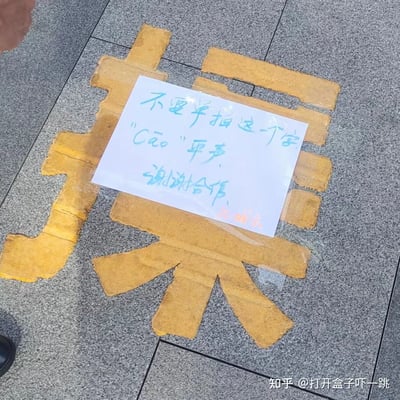 图片展示了灰色地砖地面上，用黄色砖块拼出的大型汉字“操”。在汉字上方贴有一张白色手写纸条，内容为：“不要单独拍这一个字 'Cāo' 平声，谢谢合作。” 右下角可见水印“知乎 @打开盒子吓一跳”。

图片中存在谐音梗与歧义防范：汉字“操”为多音字，当读第四声“cào”时可能带有粗俗含义，而纸条特意标注“平声”（第一声“cāo”），意在表明此处使用的是中性含义（如“操练”“操劳”），提醒拍摄者不要单独截取该字造成误解。