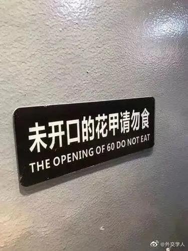 这是一张实拍的餐厅标识牌照片，标识牌为黑底白字，中文提示为“未开口的花甲请勿食”，本意是提醒食客不要食用未开口的花甲（一种蛤蜊类海鲜），避免吃到不新鲜食材。但下方的英文翻译出现了严重错误，将中文里可指代60岁的“花甲”误解，翻译成了“THE OPENING OF 60 DO NOT EAT”，完全偏离原意，形成了搞笑的翻译翻车现场。