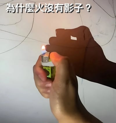 图片中一只手握着一个绿色打火机，打火机正点燃着蓝色火焰。手部和打火机在白色背景墙上投下了清晰的黑色影子，但火焰本身却没有产生影子。图片顶部用白色文字醒目地写着“為什麼火沒有影子？”，引发观者对这一物理现象的思考。