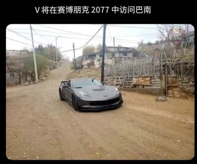 这是一张充满反差感的玩梗图片，图片上方配有文字“V将在赛博朋克2077中访问巴南”，画面主体是一辆黑色的雪佛兰科尔维特超跑行驶在重庆巴南的乡村土路上，周围是质朴的乡村民居、土路和简易围栏。《赛博朋克2077》的游戏背景是充满未来科技感、霓虹闪烁的夜之城，而图中的场景却是充满生活气息的乡村土路，两者风格形成强烈反差，制造出荒诞搞笑的效果，属于用现实场景结合游戏设定的玩梗创作。