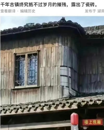 图片展示了一座具有传统木质结构和瓦片屋顶的古镇建筑，墙面部分区域露出了现代陶瓷瓷砖，形成鲜明的古今对比。上方配文“千年古镇终究抵不过岁月的摧残，露出了瓷砖”，以幽默讽刺的方式调侃古镇修复中使用现代材料（瓷砖）替代传统建材的现象，暗示所谓的“岁月摧残”实为不恰当的现代修复，引发网友对文化遗产保护方式的讨论。