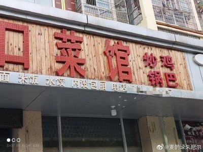 这是一张街边菜馆的招牌实拍照片，招牌以木质板材为底板，搭配醒目的红色立体大字“口菜馆”，右侧配有红色小字标注特色餐品“炒鸡 锅巴”；招牌下方用白色小字列出了提供的餐食种类：面、米饭、水饺，同时标注了“内设包厢”的服务信息，还有一处打码的联系电话。整体是朴实常见的街边餐饮店铺招牌样式，没有双关、谐音梗等特殊内容。