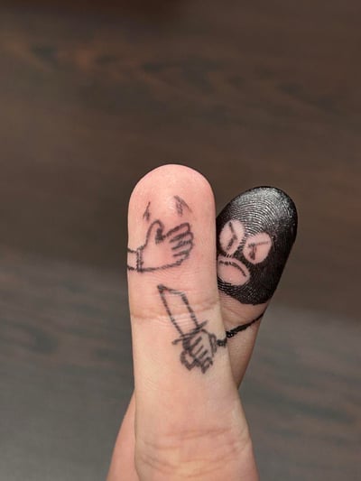 这是一幅充满创意的手指涂鸦作品，通过在两根手指上绘制图案并摆出特定姿势，模拟出歹徒挟持人质的趣味场景：一根手指的指尖被涂黑并画出愤怒凶狠的歹徒脸，另一根手指上画出被控制的手势，两者配合形成生动的挟持画面，利用手指的形态和手绘图案结合，打造出搞笑又有创意的视觉效果，没有双关或谐音梗。