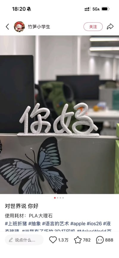 社交媒体用户“竹笋小学生”发布的一条内容，展示了其办公室桌面场景。画面中心是一个用PLA大理石材质3D打印的“你好”立体文字摆件，放置在办公桌隔板上，隔板上还贴有一只蓝黑色蝴蝶图案的贴纸。背景可见办公环境中的电脑显示器、绿色背包等物品，整体氛围偏向日常职场。配文“对世界说 你好”传递出积极的生活态度，结合#上班猪等标签，可能暗含对职场生活的轻松调侃。
