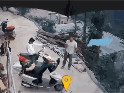 这是一段监控拍摄的动态画面，在一处户外坡道区域，有三名男子：一名男子坐在电动车后座，身体大幅向后仰，双腿抬起，姿势夸张，看起来即将从车上摔落；旁边一名穿白色上衣的男子正骑着电动车；还有一名穿灰色上衣的男子站在坡道旁，似乎被这突如其来的一幕惊到。整个场景充满了意外的滑稽感，没有双关、谐音梗等内容。