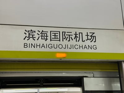 这是一张拍摄于地铁站的照片，展示了“滨海国际机场”的站名标识。标识上的中文名称正确，但对应的拼音没有按照规范将每个汉字的拼音分开，而是直接连写成了“BINHAIGUOJIJICHANG”，正常规范写法应为“BINHAI GUOJI JICHANG”，这种生硬的连写方式成为了槽点，引发网友吐槽。