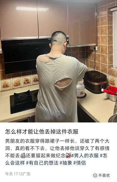 这是一张图文混排的社交媒体分享内容，上半部分为实拍场景：一名留寸头的男子背对着镜头站在自家厨房的操作台前，他身上穿的浅灰色T恤长度接近膝盖，看起来像裙子，后背还有两处明显的大破洞，衣物质感已经非常旧。下半部分是发布者的配文，发布者是该男子的女朋友，她吐槽自己实在看不下去男朋友这件破烂的旧衣服，劝说对方丢掉却被男友以穿久了有感情、要留作纪念为由拒绝，因此询问网友怎么才能让男友丢掉这件衣服，还附带了相关话题标签，内容的发布定位为广东，发布时间为当日17:12。