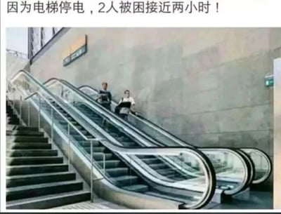 这是一张文字加注的静态单图，图上方配有文字“因为电梯停电，2人被困接近两小时！”，画面展示的是一处公共场所的自动扶梯，扶梯上有两位行人，而扶梯的左侧就是可供正常通行的步行楼梯。这是一个利用概念混淆制造笑点的梗图：封闭的升降电梯停电后会困住人，但自动扶梯停电后完全可以当作普通楼梯行走，图中的两人明明有旁边的楼梯可以通行，却被配文描述为“被困”，这种荒诞的反差感形成了搞笑效果。