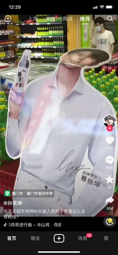 这是一张抖音短视频的截图，画面核心是超市货架旁蔡徐坤代言康师傅「喝开水」的人形立牌，立牌的头部被人为弄断，呈现出「断头」的滑稽状态。发布该视频的抖音用户@孙笑坤配文：「今天去超市坤坤的头被人弄断了是谁这么没有树枝？」，其中「树枝」是「素质」的谐音梗，属于玩梗吐槽的内容。背景是摆满饮料的超市货架，视频界面显示点赞2021、评论1095、收藏87、转发924，定位在厦门市莲河中学，BGM为《鸡哥进行曲》，进一步强化了和蔡徐坤相关的玩梗氛围。