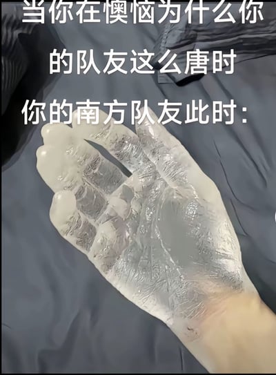 图片上方有白色文字：'当你在懊恼为什么你的队友这么唐时 你的南方队友此时：'，下方是一只手的特写，手部皮肤因寒冷显得苍白僵硬，纹理清晰，背景为灰色床单。图片通过幽默方式暗示南方队友因天气寒冷导致操作失误，解释其游戏表现不佳的原因，其中'唐'可能为'坑'的谐音或方言表达，增加趣味性。
