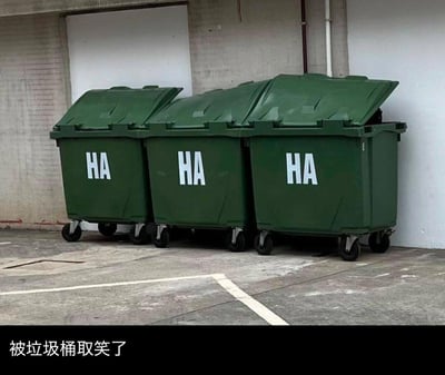 图中展示了三个并排靠墙摆放的绿色带轮大型垃圾桶，每个桶身都印有白色的大写字母“HA”，三个“HA”连起来就组成了拟声词“HAHAHA”（哈哈大笑）。图片下方配有中文文字“被垃圾桶取笑了”，通过拟人的手法，将无生命的垃圾桶赋予了“嘲笑”的人格，制造出一种被日常物品调侃的搞笑反差感。
这是利用了拟声词的组合梗，把三个独立的“HA”解读为连续的大笑，让普通的场景变得趣味十足。
