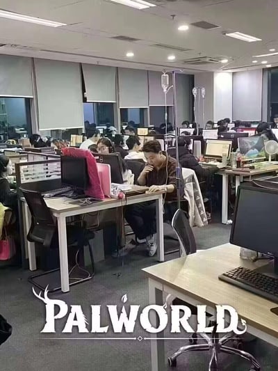 这是一张经过改编的职场梗图，画面展示了一个灯火通明、工位密集的办公区，大量员工在深夜仍忙碌于电脑前，前景处的员工一边打着吊瓶一边工作，呈现出极致高强度的加班状态；图片底部添加了爆火游戏《Palworld》（幻兽帕鲁）的白色官方logo，以此调侃这款游戏爆火背后，外界猜测的开发团队“带病加班”的高压处境，用夸张的场景讽刺了职场中“996”“极限加班”的不合理现象。