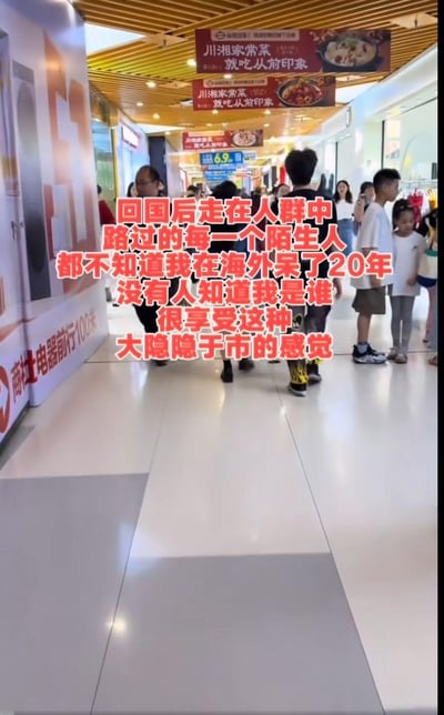 这是一张竖屏短视频截图，画面呈现了热闹的室内商场通道，往来的行人穿梭其中，左侧有商社电器的指引标识，上方悬挂着“从前印象”餐厅的宣传牌。图中用醒目的红色大字叠加了一段作者的感悟：“回国后走在人群中，路过的每一个陌生人都不知道我在海外呆了20年，没有人知道我是谁，很享受这种大隐隐于市的感觉”，表达了作者结束20年海外生活回国后，享受在人群中匿名、淡然生活的惬意心情。图中没有双关、谐音梗或暗示内容。