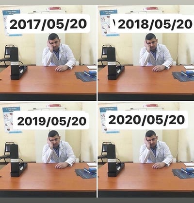 这是一张2x2的多图拼接照片，展示了同一男子在2017年5月20日、2018年5月20日、2019年5月20日和2020年5月20日的相同场景。男子身穿白色外套，坐在木质办公桌前，左手撑着头，右手放在桌面上，背景为浅色墙壁，桌上有黑色设备和蓝色物品。四年间场景几乎完全一致，仅时间变化，形成强烈的重复感和时间流逝的对比。