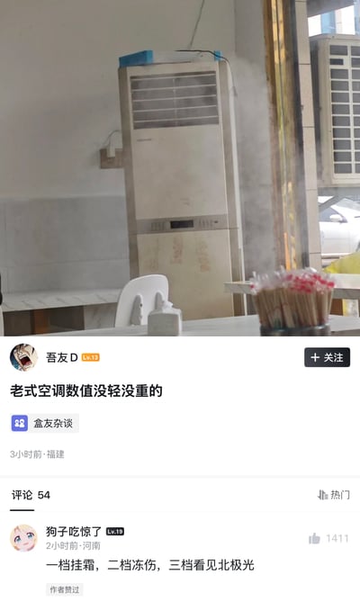 该内容由上半部分实拍图和下半部分社交平台帖子组成，实拍部分展示了室内一台老旧的立式空调，出风口正大量涌出白色冷气，直观体现出其制冷效果极强；下半部分是社区帖子内容，发布者“吾友D”配文吐槽老式空调制冷力度难以把控，热门评论区用户用极度夸张的表述调侃老式空调制冷过猛，内容幽默有共鸣感。