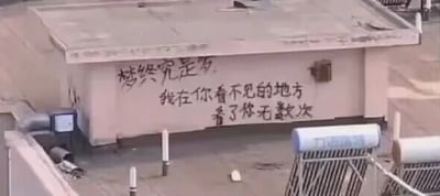 这是一张原始拍摄的横版静态涂鸦类图片，画面主体是居民楼区域一处水泥平台的墙面，墙面上用黑色颜料手写了两段抒发暗恋心事的文字：“梦终究是梦”“我在你看不见的地方看了你无数次”，文字风格随性直白。画面下方能看到太阳能热水器等居民设施，整体氛围带着青涩又伤感的情绪，是普通人将私密心事以涂鸦形式留在公共区域的记录。