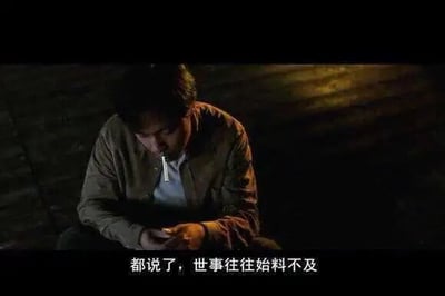 这是一张电影《不虚此行》的剧照截图，画面整体色调昏暗，营造出压抑、低落的氛围。图中是胡歌饰演的角色闻善，他低头坐着，嘴中叼着一根细长物品，神情落寞沮丧，双手交叠放在身前，似乎正沉浸在失意的情绪中。画面底部配有白色字幕“都说了，世事往往始料不及”，直白地传递出角色对人生境遇难以预料的无奈与感慨。