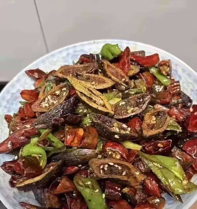 这是一张实拍的菜肴照片，菜肴盛放在带有淡蓝色花纹的白色瓷盘中，主体是被切开的干槟榔切片，搭配大量切段的干红辣椒、鲜青椒炒制而成，菜品表面撒有白芝麻，整体油润亮泽。槟榔通常作为咀嚼类嗜好品，极少被作为食材入菜炒制，因此这道菜属于非常少见的猎奇黑暗料理范畴。