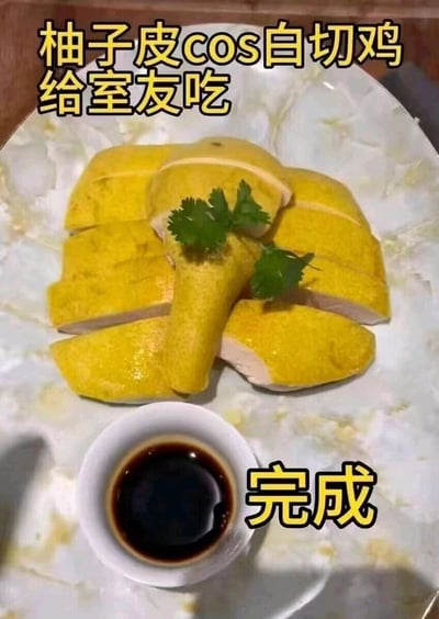 这是一张展示趣味整蛊创意的静态图片，图中处理后的柚子皮被切片摆放在盘中，造型高度模仿粤菜白切鸡的样式，还搭配了一小碗深色蘸料，从外观上极具迷惑性。图片顶部文字标注“柚子皮cos白切鸡给室友吃”，底部标注“完成”，表明这是一个为了整蛊室友而制作的伪装料理，利用柚子皮的黄色外皮和切片后的形态，巧妙模仿白切鸡的外观，充满生活趣味性和创意。