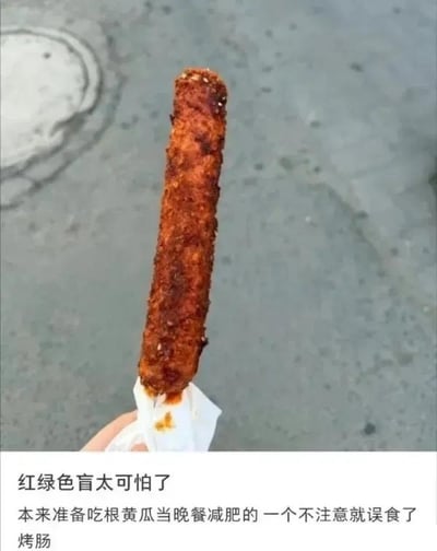 图片中一只手握着一根表面撒满芝麻、裹着红油的烤肠，背景是灰色的街道地面。下方配文幽默地讲述了一个红绿色盲者的减肥趣事：本想晚餐吃黄瓜减肥，却因分不清颜色误食了烤肠，用生活小误会制造出搞笑效果。