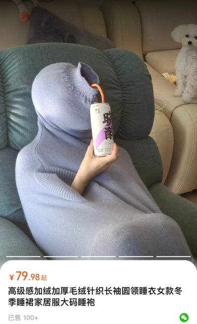 图片中，一个人坐在绿色扶手椅上，全身被一件浅紫色的加绒加厚针织睡袍包裹，只露出一只手拿着一罐印有“野醉”字样的饮料，通过吸管饮用。睡袍宽松到完全覆盖头部，营造出慵懒舒适的冬日氛围。背景中，一只白色的小狗安静地坐在米色沙发上，增添了居家的温馨感。图片底部是产品信息：“¥79.98起 高级感加绒加厚毛绒针织长袖圆领睡衣女款冬季睡裙家居服大码睡袍 已售100+”，显示这是一款冬季女士家居服的商品展示图。