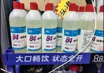 这是一张实拍的商超货架照片，货架的蓝色陈列栏上印着原本用于饮品宣传的白色大字“大口畅饮 状态全开”，但栏上摆放的却是多瓶红盖、瓶身带有蓝白标签的84消毒液，消毒液每瓶净含量500g，旁边贴有黄色爆炸形价格标签标注“5元2瓶”。原本用于鼓励饮用饮料的标语和具有强腐蚀性、绝对不能饮用的84消毒液放在一起，形成极强的反差搞笑效果，还存在误导消费者的风险。