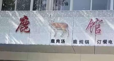 这是一张线下餐饮店铺招牌的实拍图，招牌底板为带孔洞的金属质感材质，上方以红色和紫红色字体分别呈现“鹿”“馆”二字，中间搭配一只写实风格的站立梅花鹿图案，明确店铺主题。下方分栏标注了店内主打菜品“鹿肉汤”“鹿炖锅”，还有未显示完整的“订餐电”字样，整体设计简洁直观，清晰传递出店铺以鹿肉相关菜品为特色的餐饮定位。