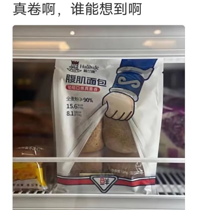 图片展示了冰箱冷藏层中的一袋海沃德牌“腹肌面包”，包装袋上印有卡通手臂撕开包装的图案，露出两块棕褐色的面包。图片上方配有文字“真卷啊，谁能想到啊”，表达对“腹肌面包”这一产品命名的惊讶与调侃。产品包装标注“全麦粉≥90%”“15.6g蛋白质/100g”“8.1g膳食纤维/100g”等信息，结合“腹肌”名称，暗示健康、健身属性，反映出食品行业在产品命名上的内卷现象。