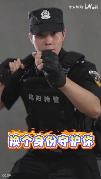 这是一张来自bilibili平台官方账号“平安绵阳”的宣传视频截图，画面中一位身着全套黑色特警装备的女特警，双手摆出格斗戒备的姿势，面部神情严肃专注，展现出专业干练的气质。画面底部带有火焰特效的醒目文字“换个身份守护你”，传递出特警队伍以不同身份守护群众安全的暖心决心，整体风格硬核又充满正能量。