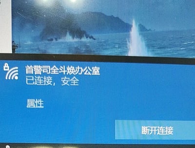 这是一张电脑屏幕的翻拍截图，展示了Windows系统的WiFi连接状态窗口：当前已连接的WiFi名称为“首警司全斗焕办公室”，窗口标注“已连接，安全”，下方设有“属性”选项和“断开连接”按钮。窗口上方的背景是一段海战相关的动态画面，可见海面、被击中溅起的水柱以及远处的岛屿，推测是正在播放的海战类影视或游戏内容。整个截图的趣味点在于使用了带有恶搞性质的WiFi名称，制造出反差感。