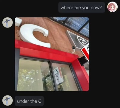 图片展示了KFC餐厅的外观，红色与砖面墙的建筑上有一个显眼的白色大写字母'C'。图片上方叠加了聊天界面，粉色头发的动漫风格头像发送消息'where are you now?'，下方回复'under the C'。通过文字与场景结合制造幽默效果，利用餐厅招牌上的'C'字母玩文字游戏，暗示自己在KFC餐厅附近。