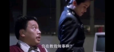 这是一张来自香港电影《逃学威龙2》的截图，画面左侧是演员吴孟达饰演的警察曹达华，他眼睛瞪大、嘴巴微张，露出惊讶又带着自负与不满的神情，抬头看向画面右侧身着警服的女性角色；右侧的女性角色低头，姿态恭敬。画面下方配有白色字幕“你在教我做事啊？”，这句话充满了对他人指教的反感与不服，后来成为网络热梗，常被用来回怼那些越界、多管闲事的指教，在职场或日常交流场景中被广泛使用，用来表达自己对被指手画脚的不满。