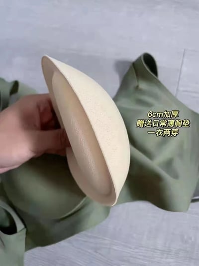 图片中一只手正拿着一个米白色的6cm加厚胸垫，胸垫质地看起来较为厚实，表面有细密纹理。胸垫下方放置着一件绿色的内衣，整体场景简洁，突出产品细节。右侧配有黄色文字标注“6cm加厚 赠送日常薄胸垫 一衣两穿”，清晰传达产品的加厚特性、附加赠品及多功能穿着优势，疑似用于内衣产品的宣传展示。