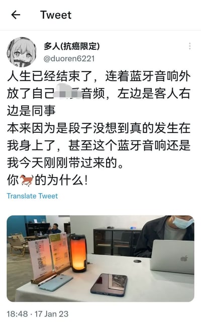 这是一张X.com（原Twitter）帖子的截图，用户“多人(抗癌限定)”(@duoren6221)分享了自己遭遇的社死瞬间：在有客人和同事在场的情况下，蓝牙音箱意外外放了自己的私密音频（部分内容被模糊处理），而这个音箱还是当天刚带来的。帖子文字充满崩溃情绪，配文“人生已经结束了”“你🐎的为什么！”。下方附带一张现场照片，显示办公桌上的蓝牙音箱、手机、MacBook，以及一位戴口罩的人。整个场景真实还原了尴尬事件的发生环境。