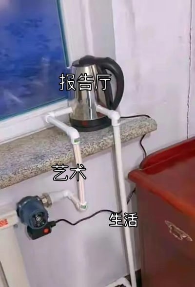 这张图用PVC水管搭建出类似人形的支架，将电水壶放置在支架的「上半身」位置并标注「报告厅」，水管的「手臂」部分标注「艺术」，下方连接的插线板与水管「下半身」标注「生活」。通过这种日常物品的组合，具象化地隐喻了「生活是基础，艺术作为连接，通向精神文化层面（报告厅代表精神/文化场景）」的关系，把抽象的概念用趣味的实物结构呈现，创意十足又充满笑点。