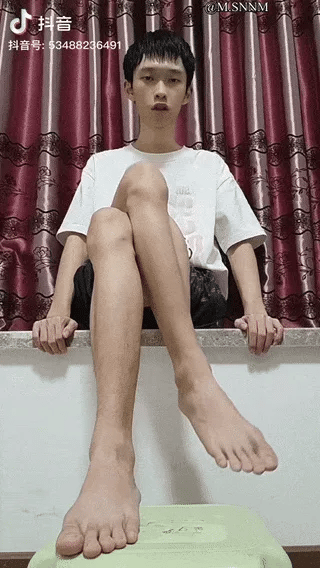 这是一段来自抖音平台的动态GIF图，图中男子坐在室内的台面上，将一只脚踩在前方的浅绿色凳子上，另一只脚巧妙地贴合在踩凳子的脚后方，通过精准的肢体摆放和拍摄视角，制造出自己只有一只脚的视觉错觉，画面充满趣味性，利用视角偏差打造出新奇的搞笑效果。
