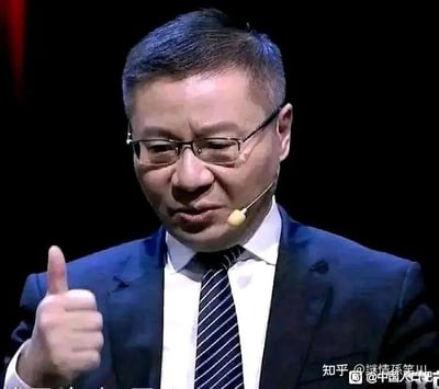 这是学者张维为在公开演讲场合的视频截图，他戴着眼镜，身着深色西装、白衬衫与条纹领带，佩戴着耳麦，眉头微皱，同时竖起右手大拇指。这个画面被网友截取制作成表情包，在网络上用来表达认可、赞同，或是带有调侃意味的肯定，适用于各类需要表达支持态度的社交场景。