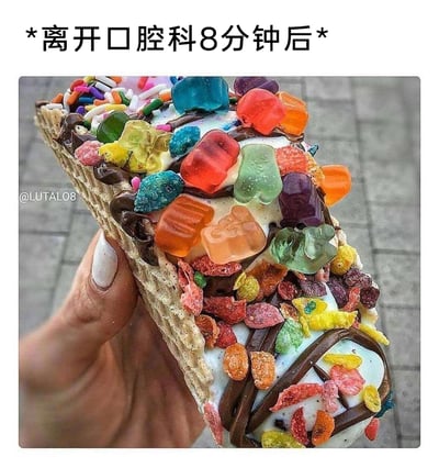 这是一张充满生活趣味的搞笑梗图，顶部标注文字“*离开口腔科8分钟后*”，画面中一只手握着一个华夫饼底的甜点，甜点表面覆盖着白色糖霜，淋有巧克力酱，还密集堆叠着多种彩色小熊软糖、彩色脆麦片等高糖糖果，视觉上极具冲击力。这张图用夸张的方式调侃了很多人在看完牙医、被医嘱控制糖分摄入后，转头就忍不住“报复性”食用高糖食物的真实心态，引发网友的共鸣，充满搞笑氛围。