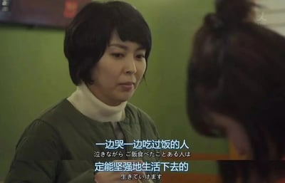 这是一张日剧《四重奏》的影视截图，画面呈现室内场景，背景是绿色墙面，左侧是穿着绿色夹棉外套内搭白色高领的短发女性卷真纪，她神情温和认真，正注视着右侧低头的女性，似乎在给予对方安慰。图片带有中日双语字幕，中文内容为“一边哭一边吃过饭的人，定能坚强地生活下去的”，日文是对应的翻译，这句台词是剧中的经典治愈内容，传递出在失意困境中依然好好对待自己、就能继续坚强生活的温暖人生感悟，整体氛围细腻又治愈。