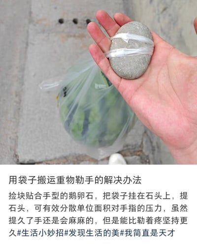 该图为图文混排的生活内容分享图，上半部分为实拍场景：一只手握着一块用透明胶带绑着塑料袋提手的鹅卵石，鹅卵石下方挂着装有西瓜的塑料袋，背景为户外水泥地面；下半部分为文字说明，介绍了通过手握鹅卵石提挂在石头上的重物，分散手指受到的压力、缓解塑料袋勒手的小技巧，同时附带了相关话题标签，文案还带有自嘲式的趣味表述。