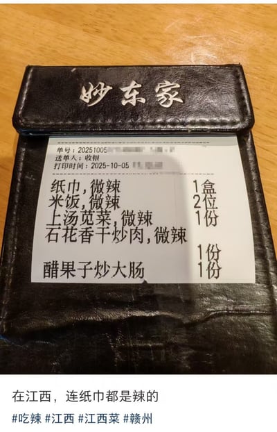 整张图为实拍图文内容，上方是放置在印有“妙东家”字样的黑色皮质餐单夹上的点餐小票，小票显示打印时间为2025年10月5日，点单内容中除了常规菜品外，纸巾、米饭都被标注了“微辣”属性；图片下方配文“在江西，连纸巾都是辣的”，并附带相关话题标签，用夸张的调侃方式体现江西菜系普遍偏辣、当地嗜辣的饮食文化特色，笑点在于点餐系统错误将非食品的纸巾也打上了微辣的口味标注，放大了江西菜无处不辣的特点。