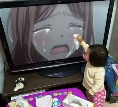 一个幼儿站在电视机前，正伸手用纸巾擦拭屏幕上哭泣的动漫女孩的眼泪。电视屏幕上显示着一个棕色头发的动漫女孩，她双眼紧闭，泪水从眼角滑落，嘴巴微张，表情十分悲伤。幼儿穿着浅色上衣和粉色带白点的裤子，神情专注地想要帮助屏幕中的角色。电视机下方的柜子上放着一个游戏手柄，前面的紫色桌子上散落着纸巾盒和一些彩色圆形物品。这张图片展现了幼儿天真无邪的同理心，让人感到温暖可爱。