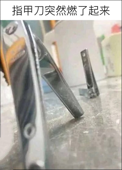 这是一张利用视觉错位打造的趣味梗图，属于顶配底文的静态单图，顶部配有文字“指甲刀突然燃了起来”。拍摄者采用极低的仰角拍摄立在台面的指甲刀，使得指甲刀的轮廓酷似站立的人形，仿佛正摆出帅气的姿势，呼应网络用语中“燃”代表热血、带感的含义，用双关的方式制造笑点，远处还能看到另一把同样立在台面上的指甲刀，整体氛围轻松搞笑。