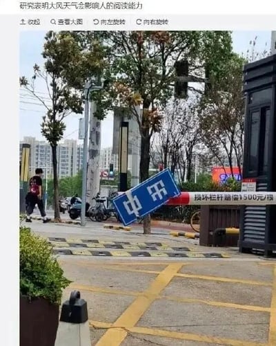 图片展示了一个大风天气下的城市街道场景，路边的“中山东路”路牌被风吹得严重倾斜，导致原本的路名文字因角度问题产生视觉误差。图片上方配有文字“研究表明大风天气影响人的阅读能力”，以幽默的方式调侃大风导致路牌倾斜，进而引发人们对文字的误读，制造出轻松搞笑的效果。