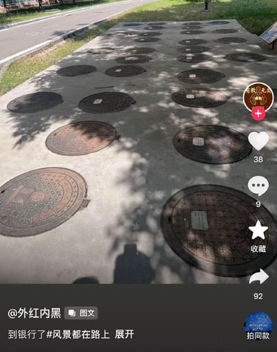 这是一张短视频社交平台的内容截图，画面主体是户外路边的水泥平地上整齐排列了数十个圆形窨井盖，规整的排列视觉效果和圆形井盖的外形很容易让人联想到银行的插卡口或者营业窗口，发布者配文“到银行了#风景都在路上”玩梗调侃。画面右侧显示该内容的互动数据：38个点赞、9条评论、92次转发，还有收藏、拍同款等功能按钮，底部标注了内容发布者的昵称。